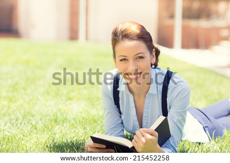 Happy student girl excited to get back to school university. Beautiful woman reading book, laying down on green grass, university campus. Student girl on university college campus park smiling happy.