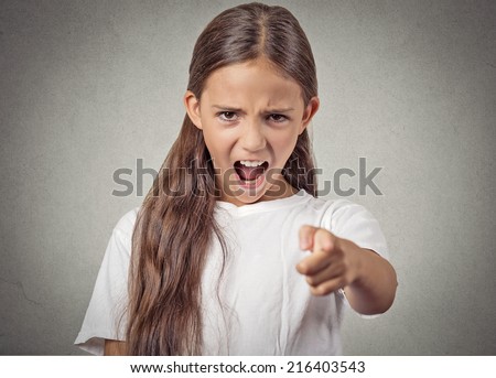 Angry child teenager girl screaming pointing finger at you demanding blaming isolated grey wall background. Negative human emotion facial expression body language attitude perception