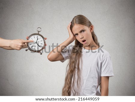 Time to go to bed. Portrait of mom showing kid clock that it is late. She doesn\'t like that, isolated grey wall background. Face expressions, emotions. Difficult parenting concept