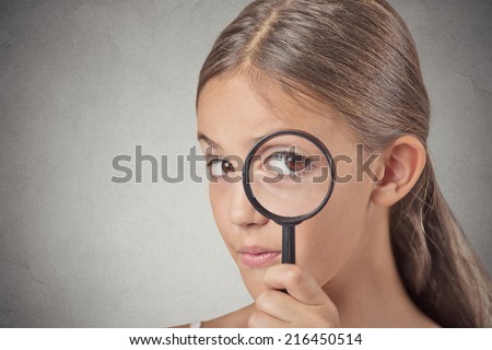 Curious. Child looking through a magnifying glass, isolated on grey wall background. Human face expressions