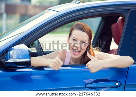 Car. Woman driver happy smiling showing thumbs up coming out of blue car side window on outside parking lot background. Beautiful young woman happy with her new vehicle. Positive face expression