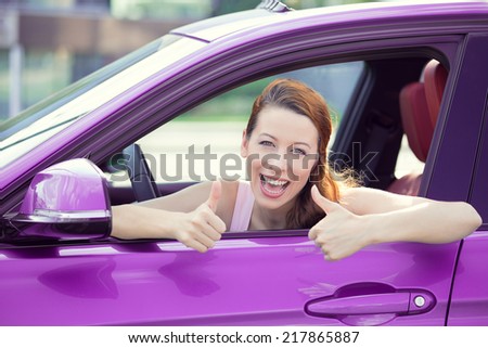 Car. Woman driver happy smiling showing thumbs up coming out of violet car side window on outside parking lot background. Beautiful young woman happy with her new vehicle. Positive face expression