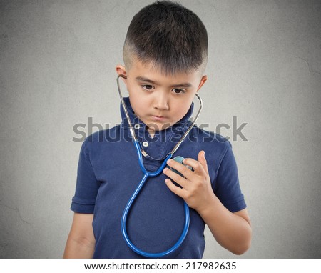 Closeup portrait child little boy listening to his heart with stethoscope isolated grey wall background. Children healthcare medical care, preventive medicine, self assessment concept. Face expression