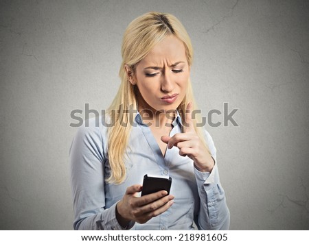 Portrait angry young business woman, mad displeased wife, pissed off employee holding mobile pointing with finger at smartphone isolated grey wall background. Negative human emotion facial expression