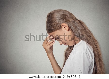 Closeup side view portrait sad tired disappointed teenager girl face on hand looking down isolated grey wall background. Negative human emotion facial expression feeling life perception body language