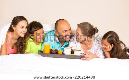 Group portrait looking happy smiling joyful family, mother, father, daughters, son having breakfast in bed, surprise on mom day. Positive human emotions, face expressions, feelings, life perception.