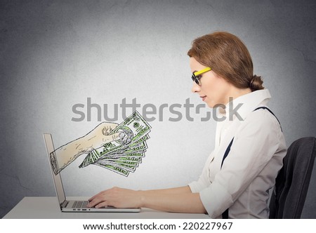 business woman with glasses working online on computer making earning money, hand with dollar bills banknotes coming out of laptop screen, isolated grey wall office background. Human face expression