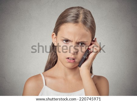 Closeup portrait headshot teenager girl talking on cell phone, having unpleasant, bad conversation, isolated grey wall background. Negative human emotions, facial expressions, reaction, feelings