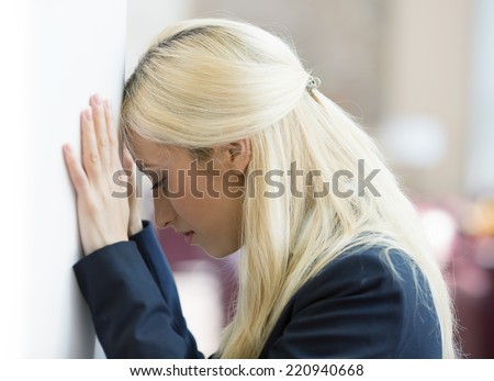Closeup portrait unhappy young business woman, head on wall, bothered by mistake having bad headache isolated background corporate office. Negative human emotion, facial expression feeling reaction