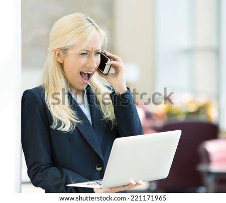 Closeup portrait upset angry unhappy woman talking screaming on phone holding computer standing in hallway corporate office. Negative human emotion facial expression feeling, life reaction. Bad news