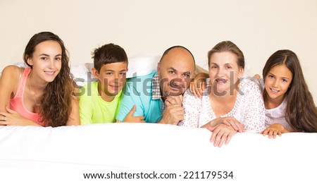 Closeup group portrait happy family, mother, father, children posing under duvet, blanket looking at camera on the bed at home, isolated room background. Positive emotions, face expressions, feelings