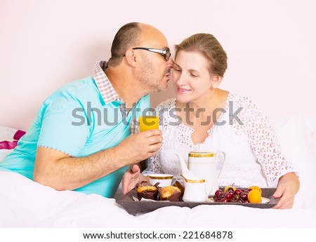 Happy, smiling middle aged couple enjoying one another while having breakfast in bed, vacation times, in hotel, house bedroom. Human emotion face expression feeling, relationship concept