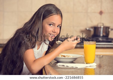 cute teenager girl eating cereal with milk drinking orange juice for breakfast in the kitchen