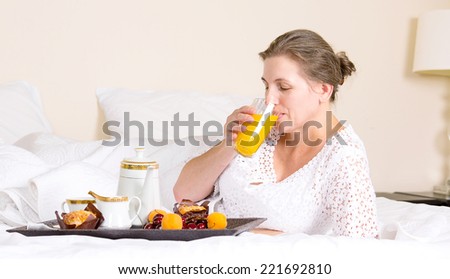 Happy middle aged, beautiful woman having breakfast, relaxing in hotel bed, bedroom of her house drinking orange juice vacation, weekend time. Positive human emotions, face expressions, feelings