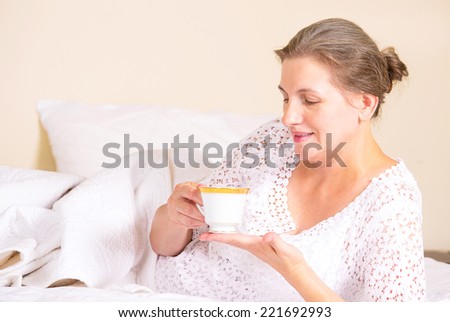 Happy middle aged, beautiful woman having breakfast, relaxing in hotel bed, bedroom of her house drinking coffee, vacation, weekend time. Positive human emotions, face expressions, feelings