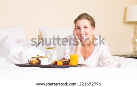 Happy middle aged, beautiful woman having breakfast, relaxing in hotel bed, bedroom of her house drinking orange juice coffee vacation, weekend time. Positive human emotion, face expressions, feelings