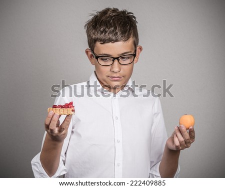 Closeup portrait young man with glasses deciding on diet, making choice sweet cookie tart fresh fruit apricot isolated grey background. Weight control eating habits. Confused face expression, emotion