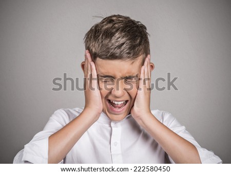 Closeup portrait stressed, frustrated, teenager boy annoyed by loud noise having panic attack screaming isolated grey background. Negative human face expression emotion feelings attitude perception