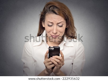 Sad stressed woman looking at her mobile cell phone isolated on grey wall background. Negative human face expressions, emotions, feelings