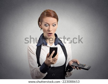 Portrait shocked businesswoman looking on smart phone holding calculator unexpected financial bills charges isolated grey wall background. Human face expression, emotion, body language, reaction