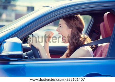Closeup portrait displeased angry pissed off aggressive woman driving car shouting at someone hand fist up in air isolated traffic background. Emotional intelligence concept. Negative human expression