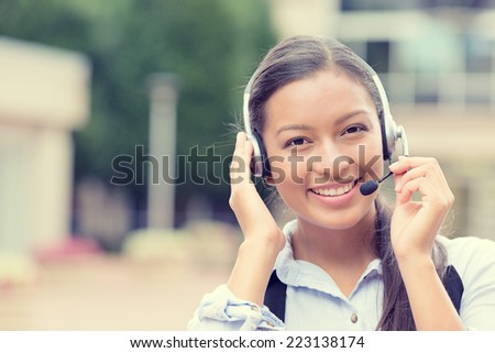 Closeup portrait smiling young female customer service representative call center agent support staff operator with phone headset isolated background with trees city building. Positive face expression
