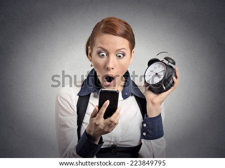 Surprised shocked business woman with alarm clock looking at smart phone with funny  face expression late for meeting isolated grey wall background. Human face expression, emotions, feelings, reaction