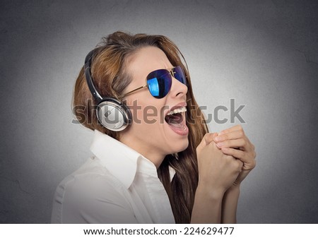 Headshot beautiful happy woman with sunglasses singing with microphone listening to music grey background. Positive human face expression emotion feeling. Happiness, holiday club disco leisure concept