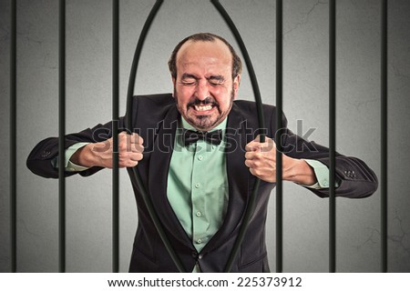 Furious strong middle aged businessman bending bars of his prison cell grey wall background. Life limitations, law violation infringement tax evasion consequences concept. Face expression emotion