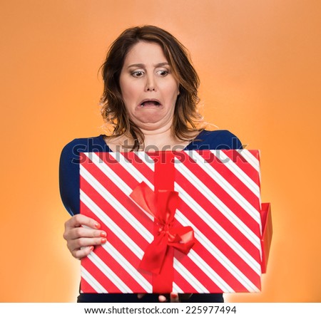Closeup portrait middle aged woman opening gift box very upset at what she received, isolated orange background. Negative human emotion, facial expression. Unsuccessful holiday shopping concept