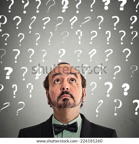 Headshot middle aged man with puzzled face expression and question marks above head looking up isolated grey wall background. Human emotion feeling body language perception problem solution concept