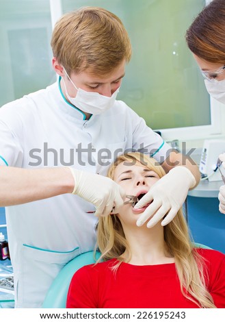Closeup young woman at dentist clinic office. Male doctor and assistant performing extraction procedure with forceps removing patient tooth. Healthcare dentistry medicine concept
