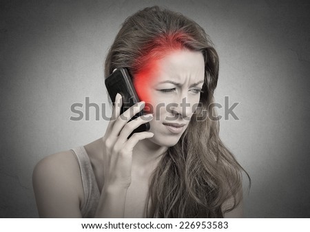 girl on the phone with headache. Upset unhappy female talking on phone isolated grey wall background. Negative human emotion face expression feeling life reaction. Cellular mobile radiation concept