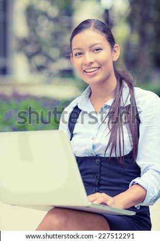 Portrait young happy business woman resting hands on computer laptop keyboard looking at camera isolated outside park with trees background. Positive face expression emotion. Technology concept