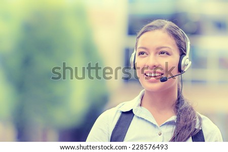 Closeup portrait smiling young female customer service representative, call center agent, support staff, operator with phone headset isolated on background with trees, city buildings. Face expression