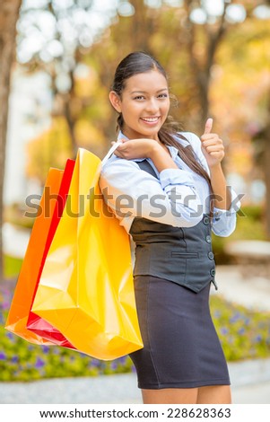 Portrait shopping excited woman showing thumbs up. Beautiful model happy smiling autumn shopper holding shopping bags walking outside isolated park trees background. Positive emotion facial expression