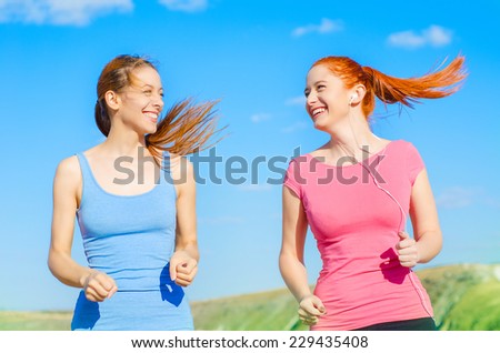 Two happy girls runners. Smiling women running outdoors on sunny day with blue sky on background training exercising. Beautiful fit multicultural fitness models in their 20s. Healthy lifestyle concept