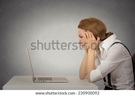 Portrait stressed young unhappy business woman working on laptop siting at desk isolated grey wall office background. Long working hours, complicated software concept. Negative face expression emotion