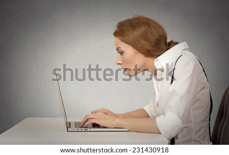 Young woman working on computer sitting at desk isolated on grey wall gloomy office background with copy space. Long monotonous tiresome working hours life concept