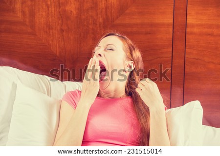 Woman yawning and stretching her arms as she lies in bed trying to wake up for a new day. Human face expression emotion body language. Lack of adequate sleep concept
