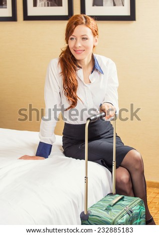 Smiling happy young business woman sitting on bed in hotel room ready for next trip. Positive face expression. Business trip traveler concept. Corporate employee entrepreneur working lifestyle