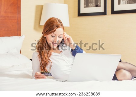 woman laying in bed smiling, with laptop computer holding credit card shopping on-line