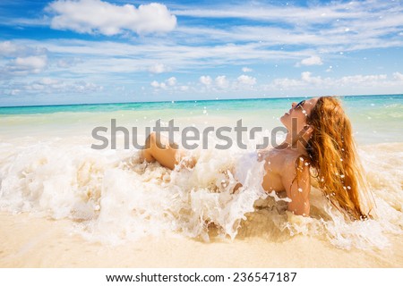 young smiling woman with sunglasses laying on beach covered in ocean waves on tropical blue sea sky background. Paradise getaway nature destination travel vacation concept. Positive face expression