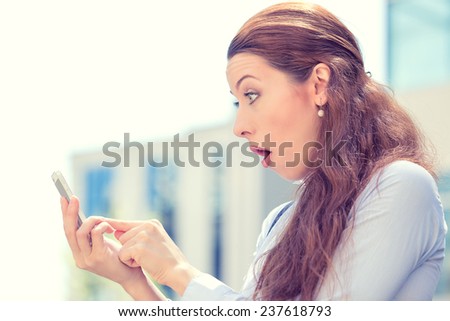 Side profile closeup portrait anxious young girl looking at phone seeing bad news or photos with disgusting emotion on her face isolated outside city background. Human emotion, reaction, expression