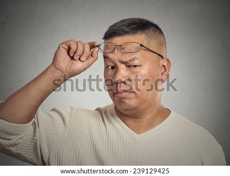 Headshot serious middle aged man with glasses skeptically looking at you isolated on grey wall background. Human face expression, body language, attitude, perception, vision