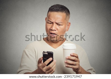 Closeup portrait serious worried middle aged man reading bad news on smart phone holding mobile drinking cup of coffee isolated grey background. Human face expression emotion. Complicated technology