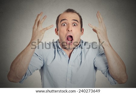 Closeup portrait headshot shocked stunned surprised young man eyes mouth wide open, hands in air yelling screaming shouting isolated grey wall background. Negative emotion facial expression feeling