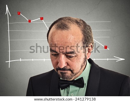 Headshot depressed stressed business man looking down financial market chart graphic going down on grey office wall background. Poor economy crisis meltdown loss concept. Face expression emotion