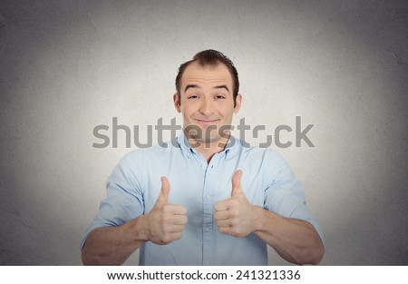 Closeup portrait super happy, excited surprised young man in blue shirt showing thumbs up sign gesture isolated grey wall background. Positive human emotion facial expression feeling attitude reaction