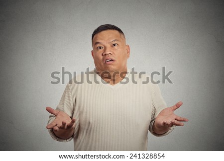 Closeup portrait dumb clueless young man arms out asking why what\'s problem who cares so what I don\'t know isolated grey wall background. Negative human emotion facial expression feeling body language